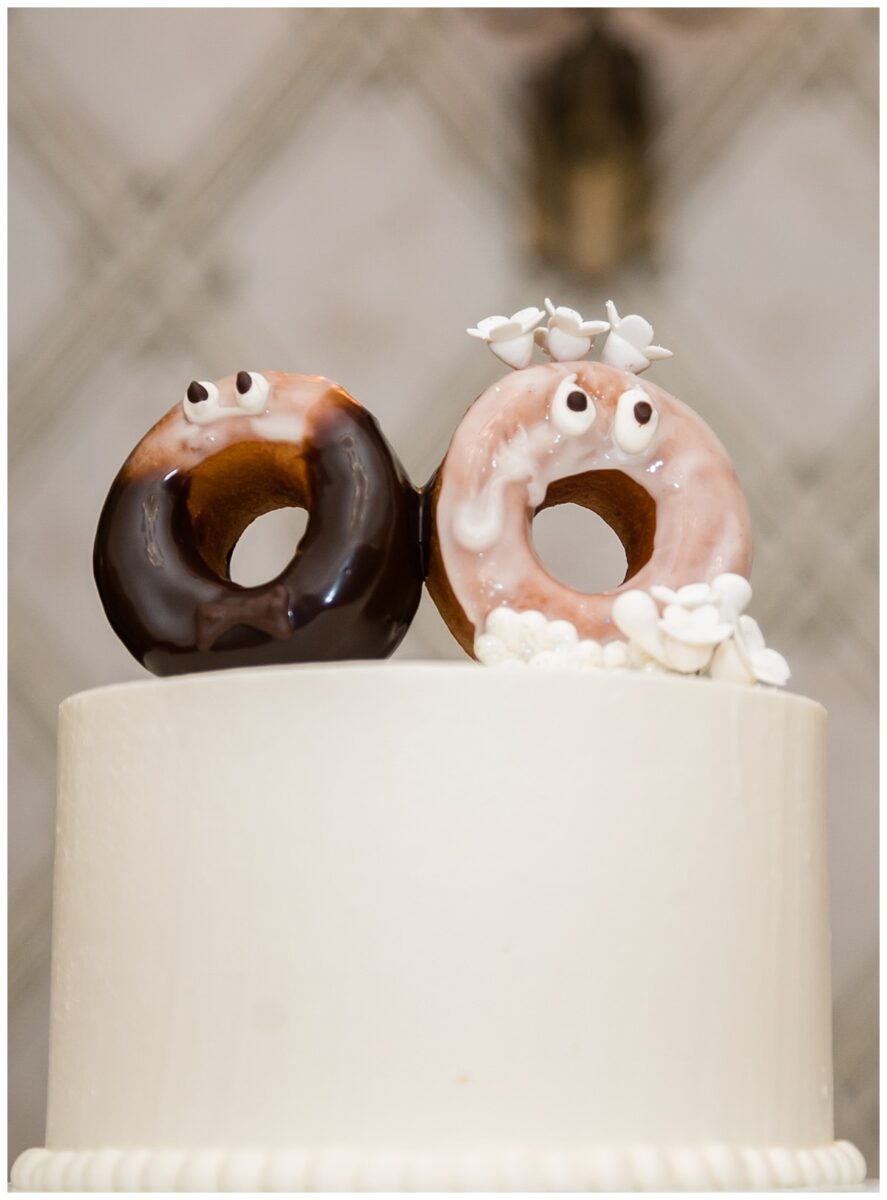 Wedding Cake Symbolism. Wedding cake top tier with the other three tiers filled with donuts. The cake topper is a pair of donuts with googly eyes. Wedding at the Rosewood Mansion on Turtle Creek in Dallas, TX.