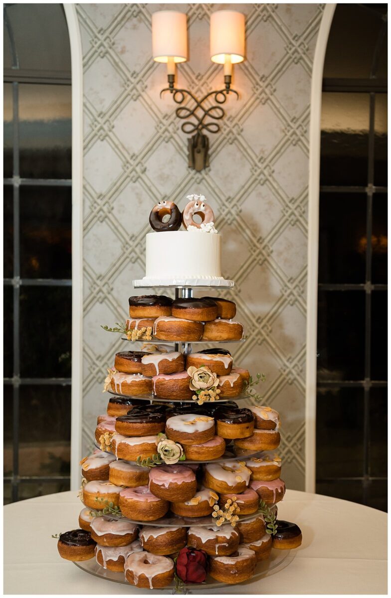 Wedding cake top tier with the other three tiers filled with donuts. The cake topper is a pair of donuts with googly eyes. Wedding at the Rosewood Mansion on Turtle Creek in Dallas, TX.
